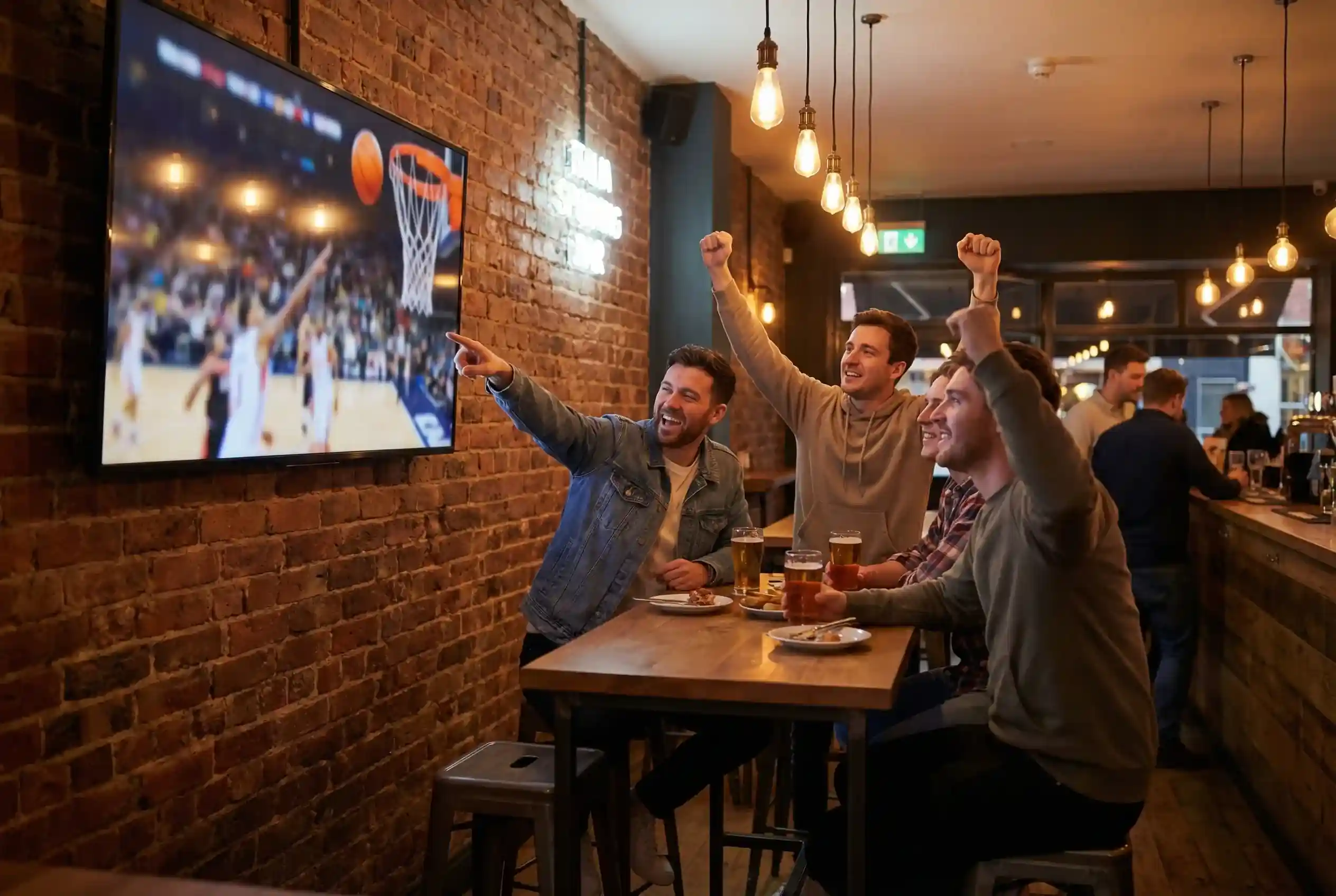 Gruppo di tifosi in un locale sportivo che guarda una partita di basket su uno schermo con espressioni di entusiasmo
